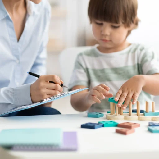 nino-jugando-juguete-de-madera-logico-en-la-oficina-de-psicologo-mujer-especialista-tomando-notas-selectivas_4_11zon